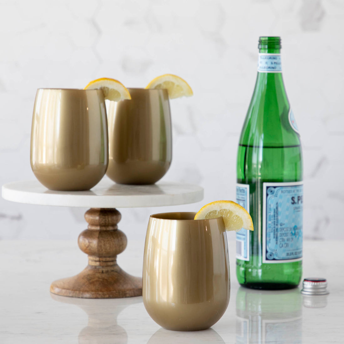 3 gold SymGlasses with lemon wedges on the rim and a bottle of water in background