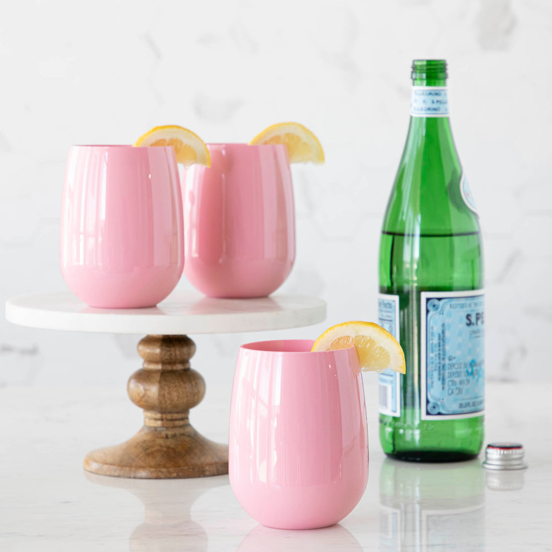 3 Pink SymGlasses with lemon wedges and a bottle of water in the background