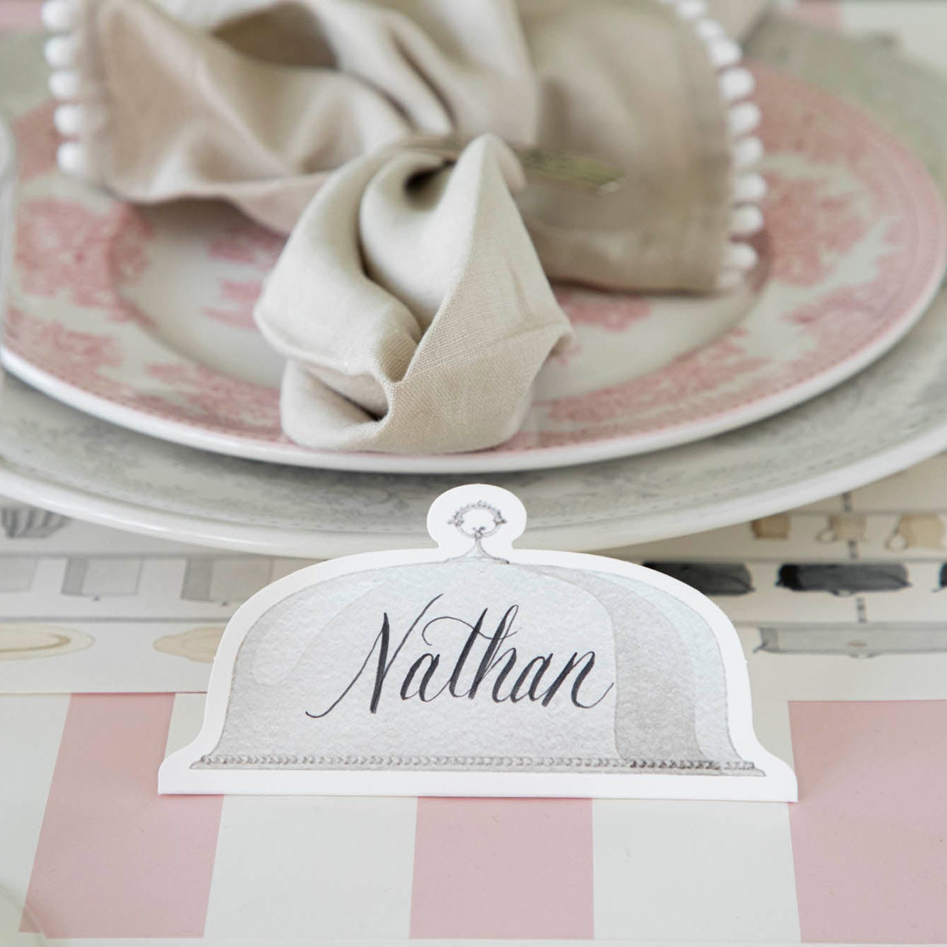 Serving Dome Place Card with &quot;Nathan&quot; written on it, in front of a place setting.