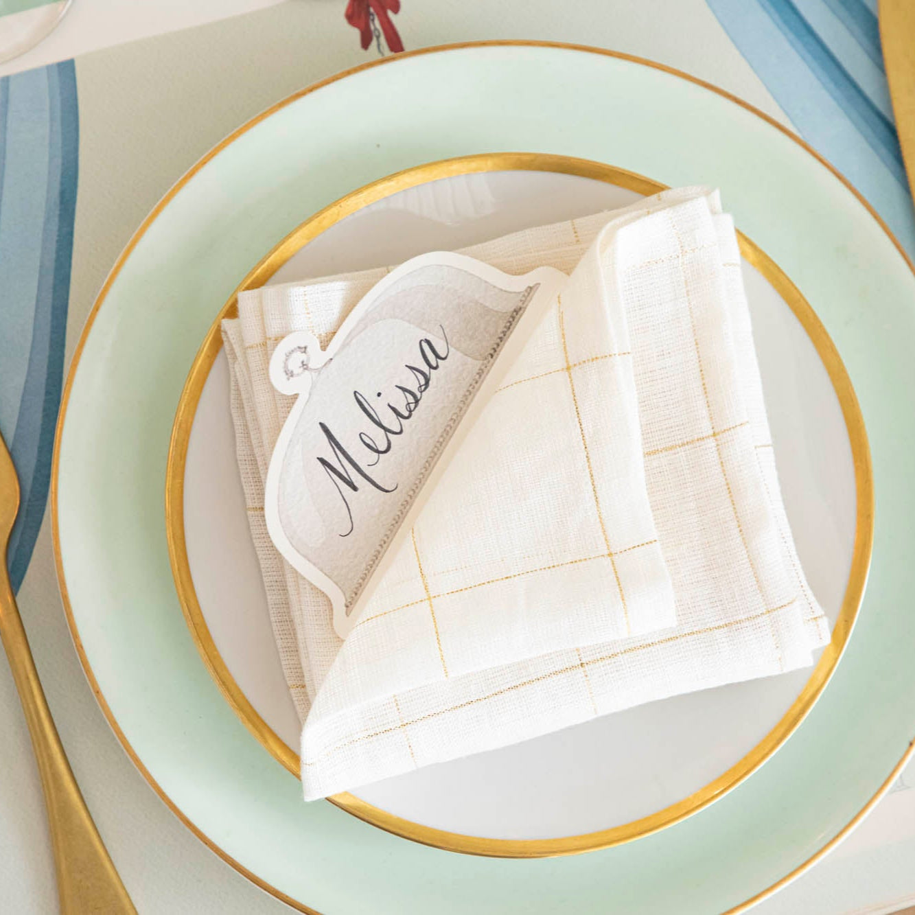 Serving Dome Place Card with &quot;Melissa&quot; written on it, resting on a folded napkin, on top of dinner plates.