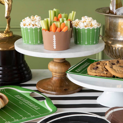 Football field and football paper baking cups filled with vegetables and popcorn on a football themed table set up.