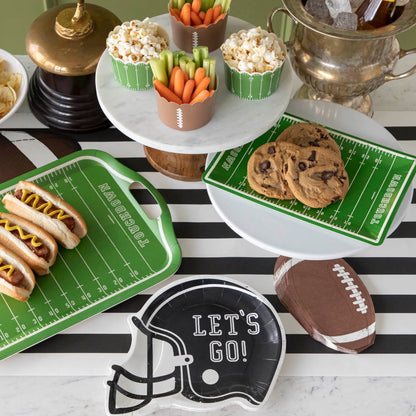 Football helmet paper plates on a football themed table setting with various game-day snacks.