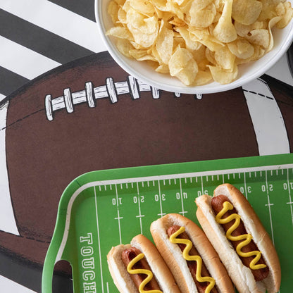 Die-cut football field placemat with a bowl of chips and tray of hot dogs on top.