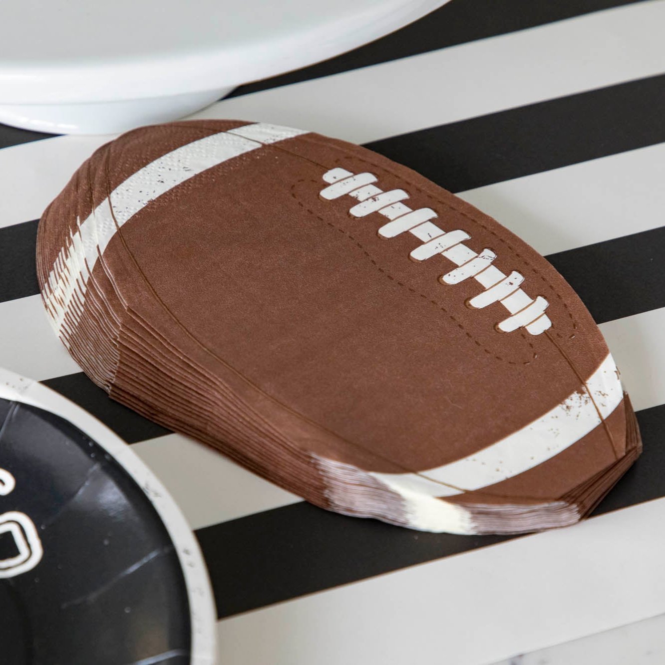 Die-cut football paper napkins on a black stripe runner.