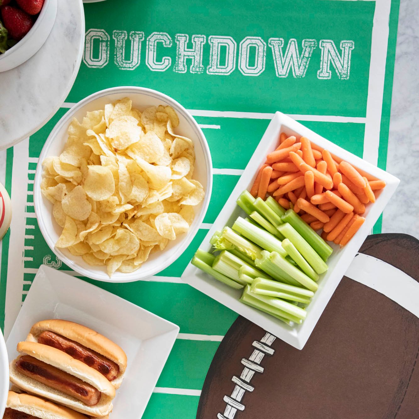 Football themed table setting featuring a Touchdown Football Field Runner with a Die-cut Football Placemat on top and various game day snacks.