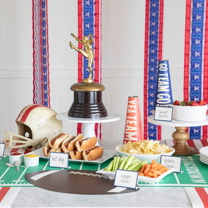 Football themed party with cookout food and a die-cut football placemat on a touchdown football field runner.