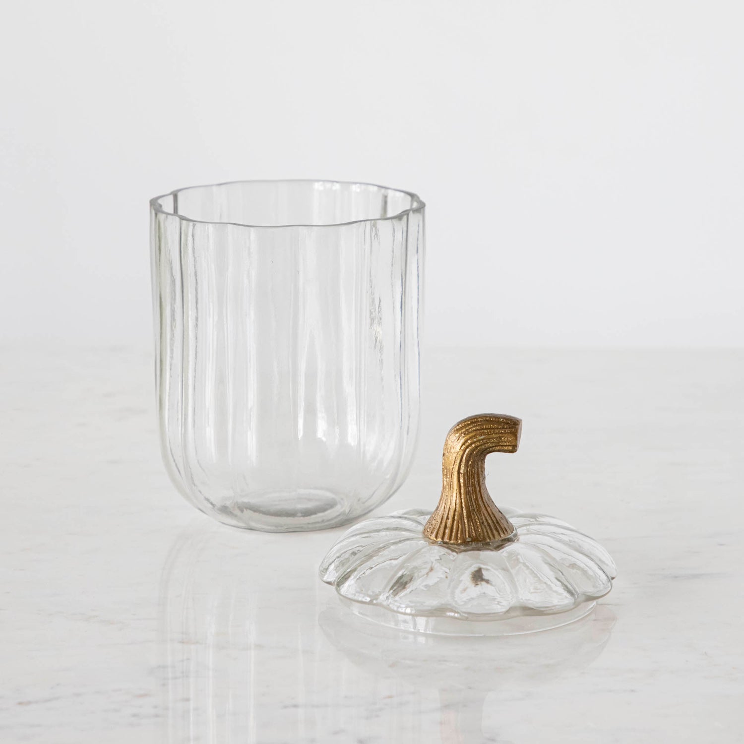 A small Translucent Pumpkin Terrarium with the antique bronze stem lid next to it, on a marble table.