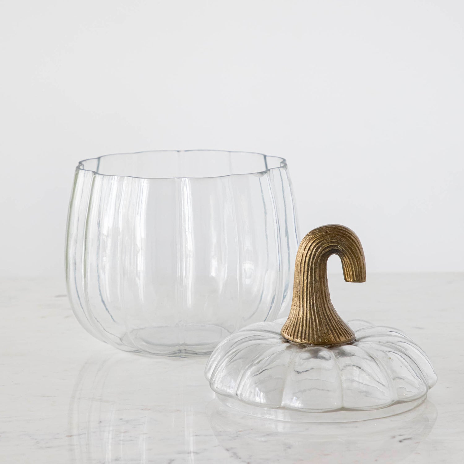 A medium Translucent Pumpkin Terrarium with an antique bronze stem lid next to it, on a marble table.