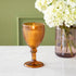 Vintage amber stemmed votive holder with a vase of flowers behind it.