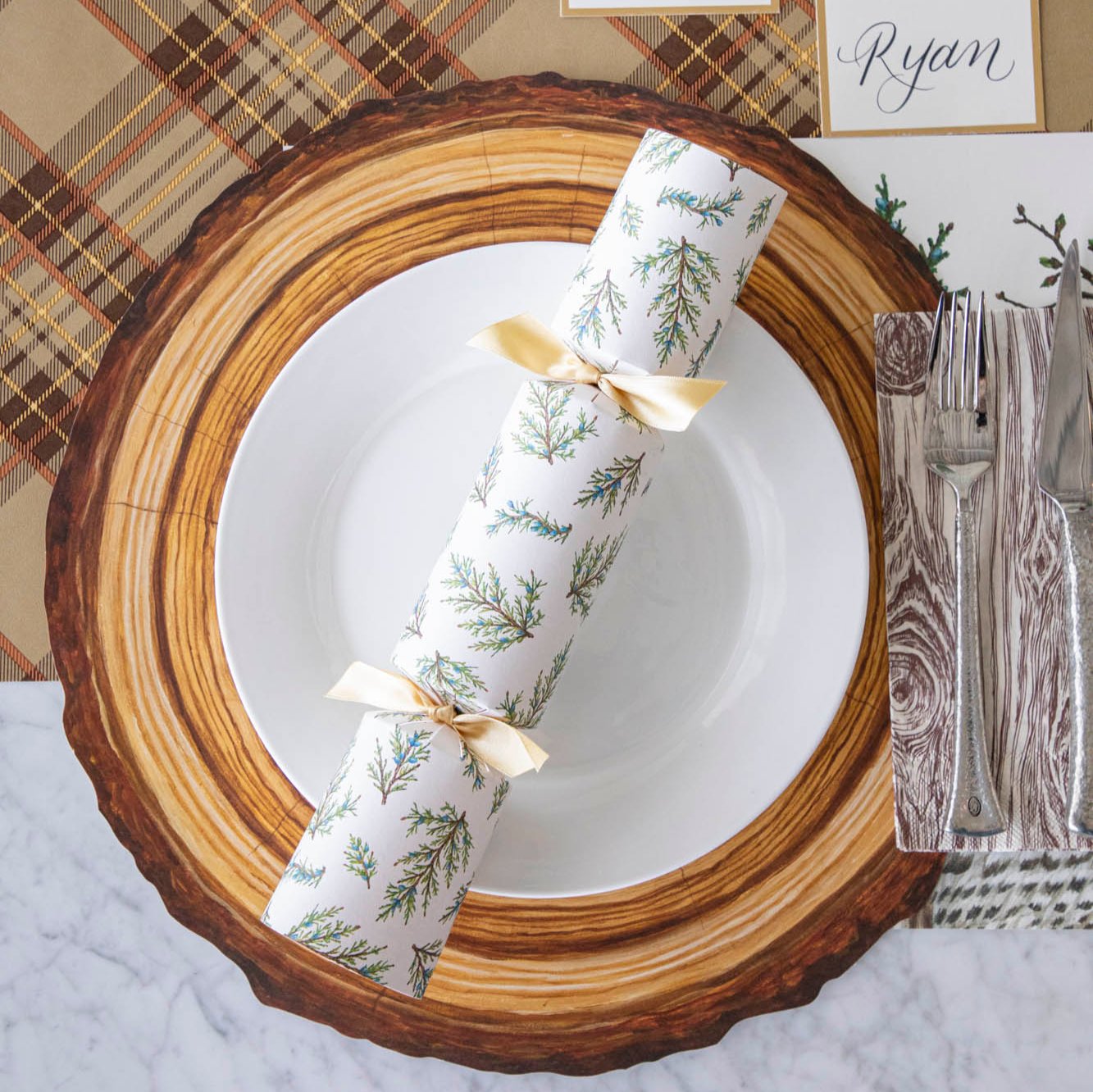 Die-cut Wood Slice Placemat with a white plate and Winter Sprigs Cracker on top and Oak napkins with silverware and an Autumn Plaid runner underneath.