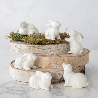 A group of Creative Co-Op Ceramic Bunnies, Set of 6, on a stack of wood.