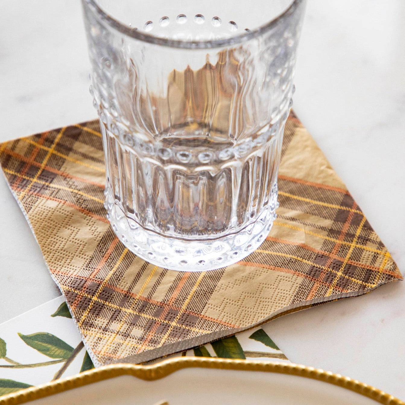 A clear glass sitting on an Autumn Plaid Cocktail Napkin in a place setting.