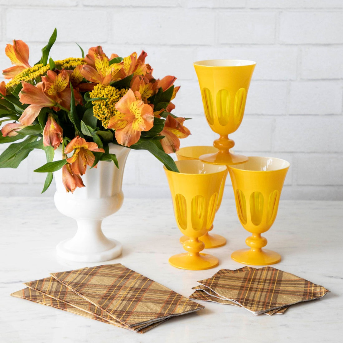 An elegant table with a flower vase and yellow glasses, with the Autumn Plaid Guest and Cocktail Napkins fanned out on the table.