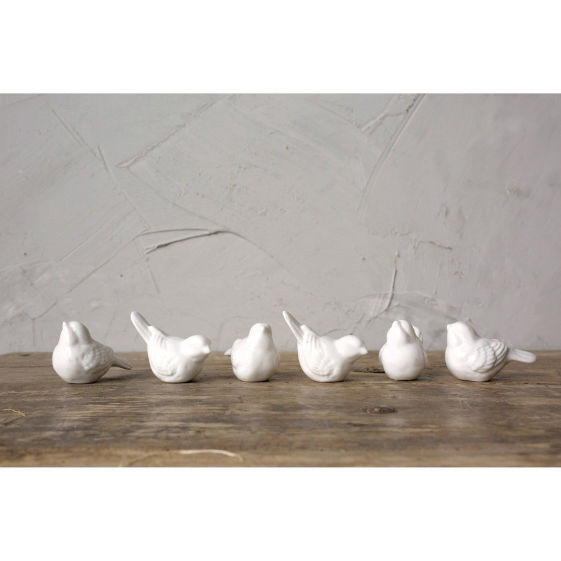 Six white ceramic birds lined up on a table.