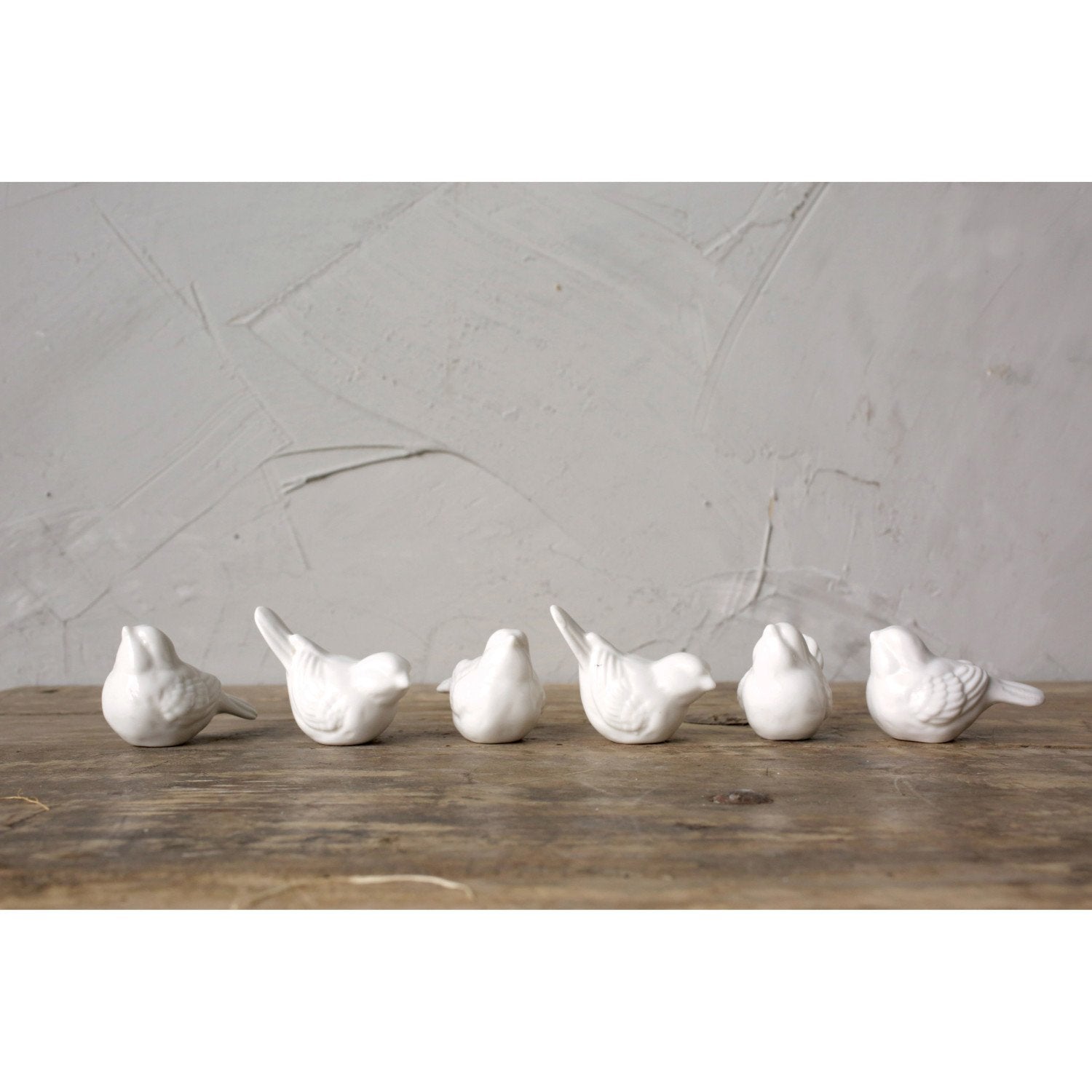 Six white ceramic birds lined up on a table.