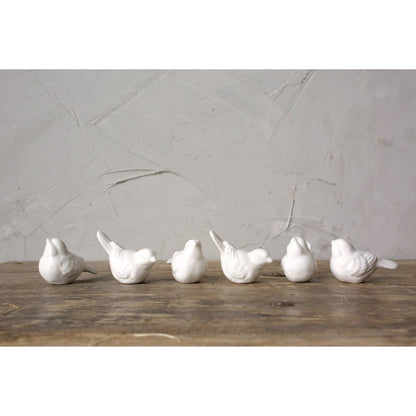 Six white ceramic birds lined up on a table.