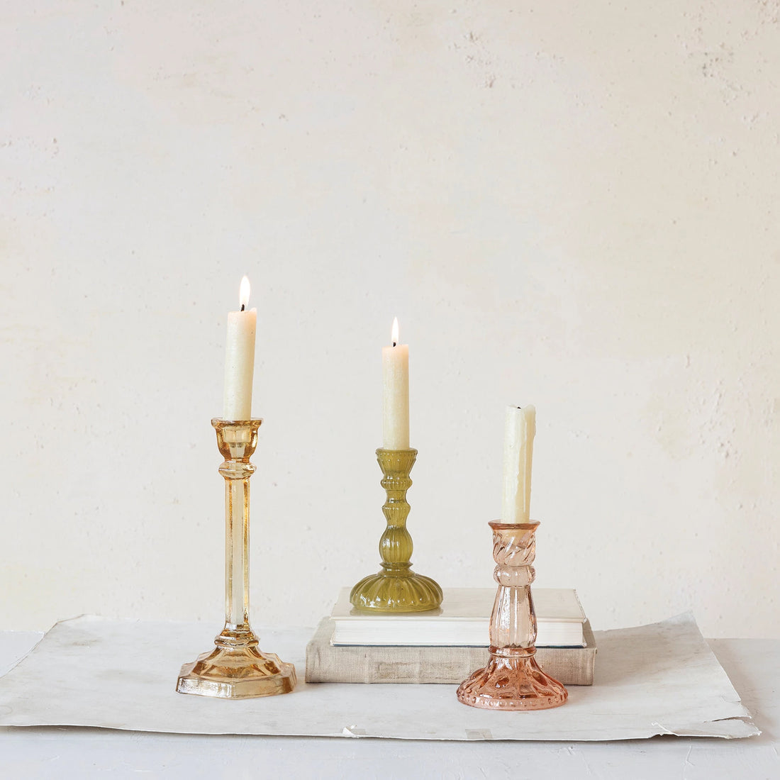 Three muted color tape candles with lit candles in them, including the Recycled Glass Taper Holder.