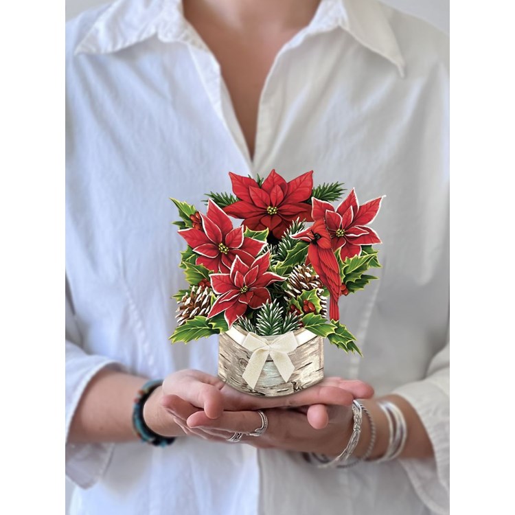 Person holding the Mini Birch Poinsettia Pop Up Card which is a bouquet of poinsettias with pinecones in a birch tree log all made of paper. 