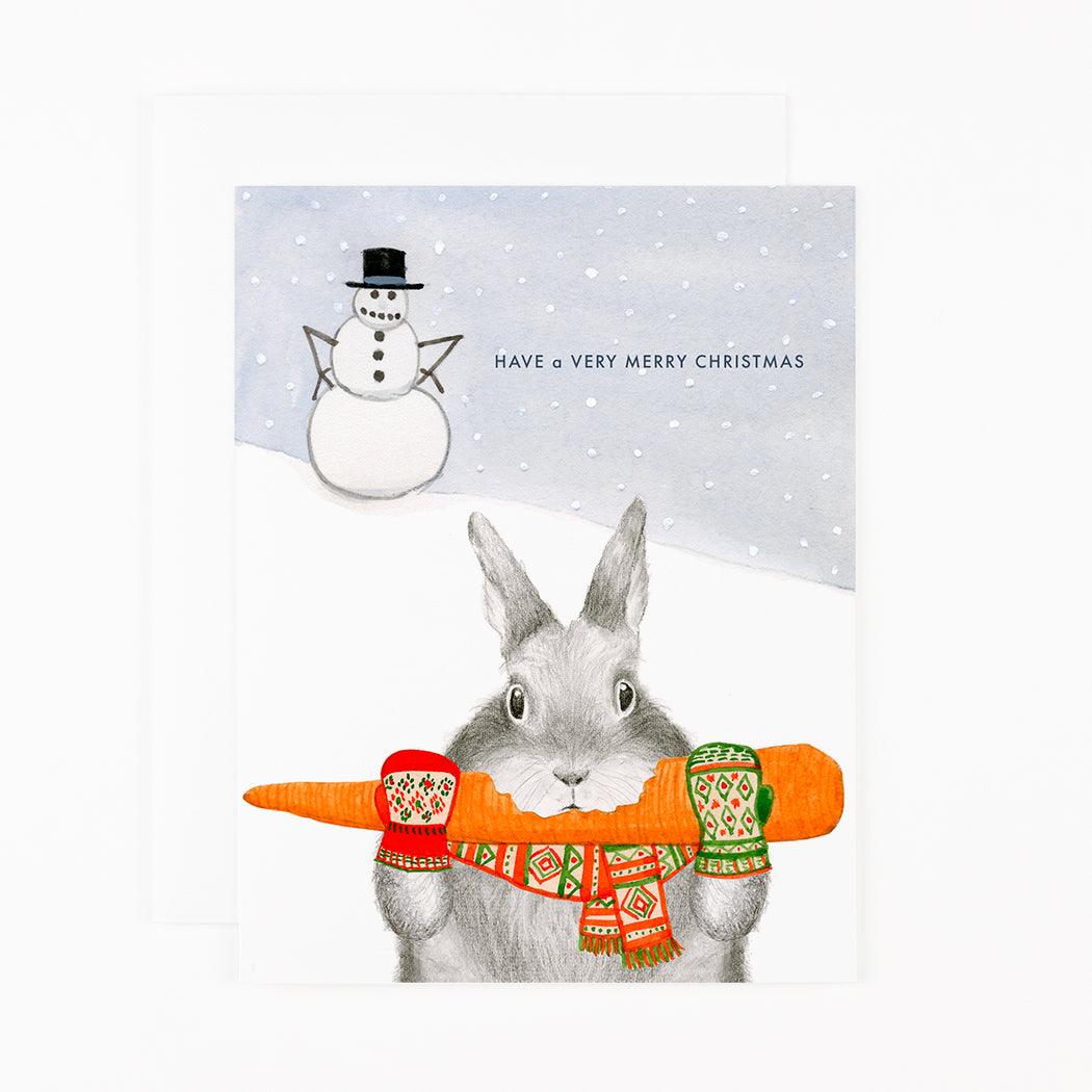 A Dear Hancock Merry Christmas card featuring an illustration of a bunny in mittens holding a carrot, with a snowman in the background, and the message &