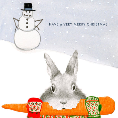 A Dear Hancock Merry Christmas card featuring an illustration of a bunny in mittens holding a carrot, with a snowman in the background, and the message &