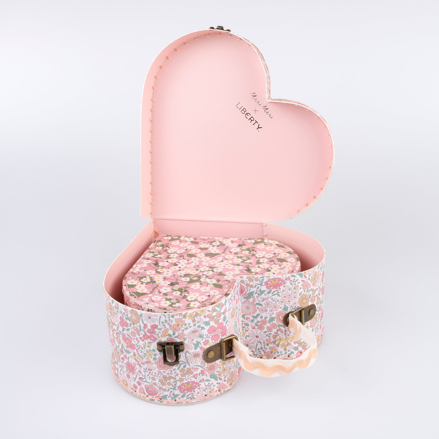 Two different sized heart-shaped suitcases made from stitched card with lamination. The smaller case can be stored inside the larger.  Each suitcase features a different Liberty floral print design, with pink tones, on the outside.