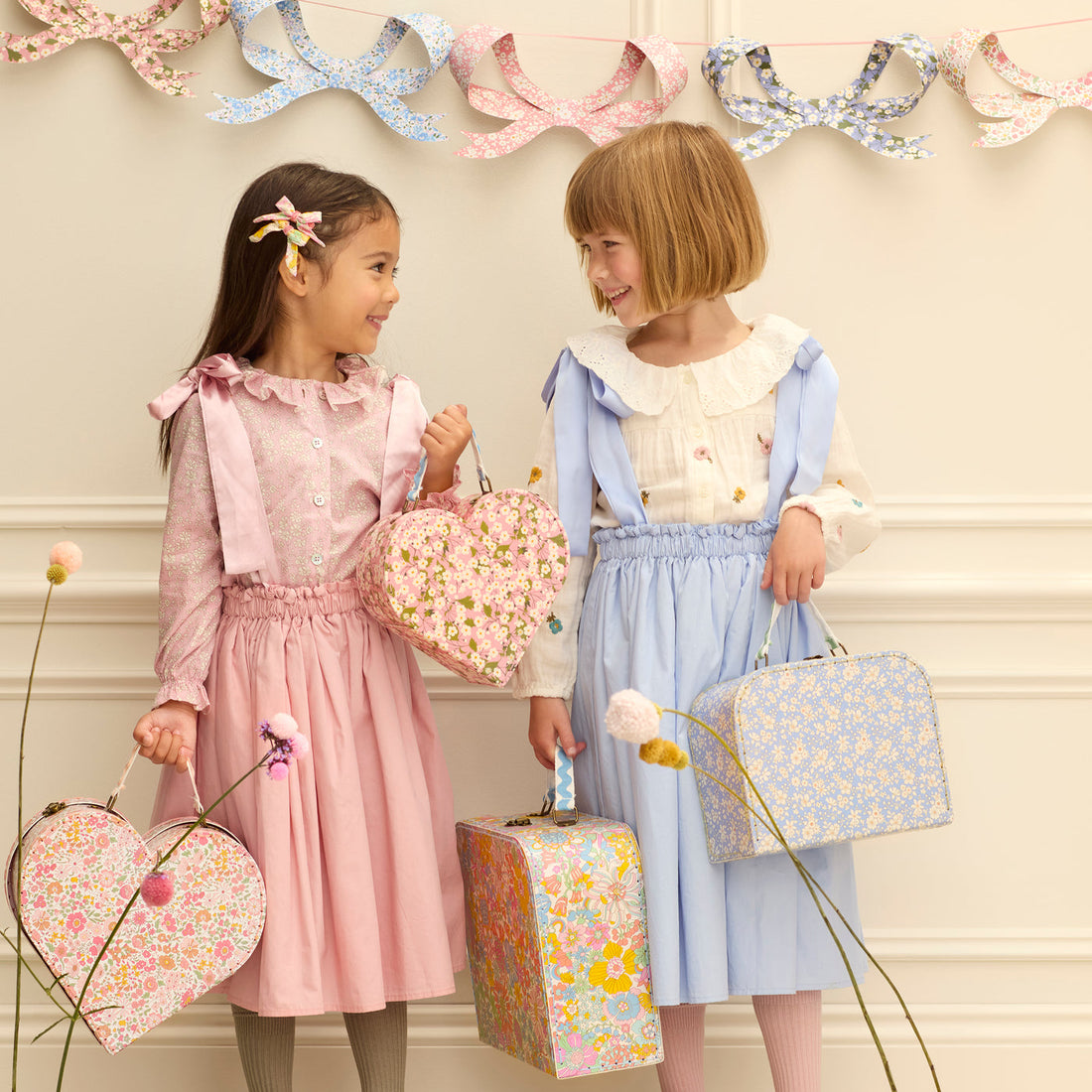 Two children holding Meri Meri x Liberty suitcases. 