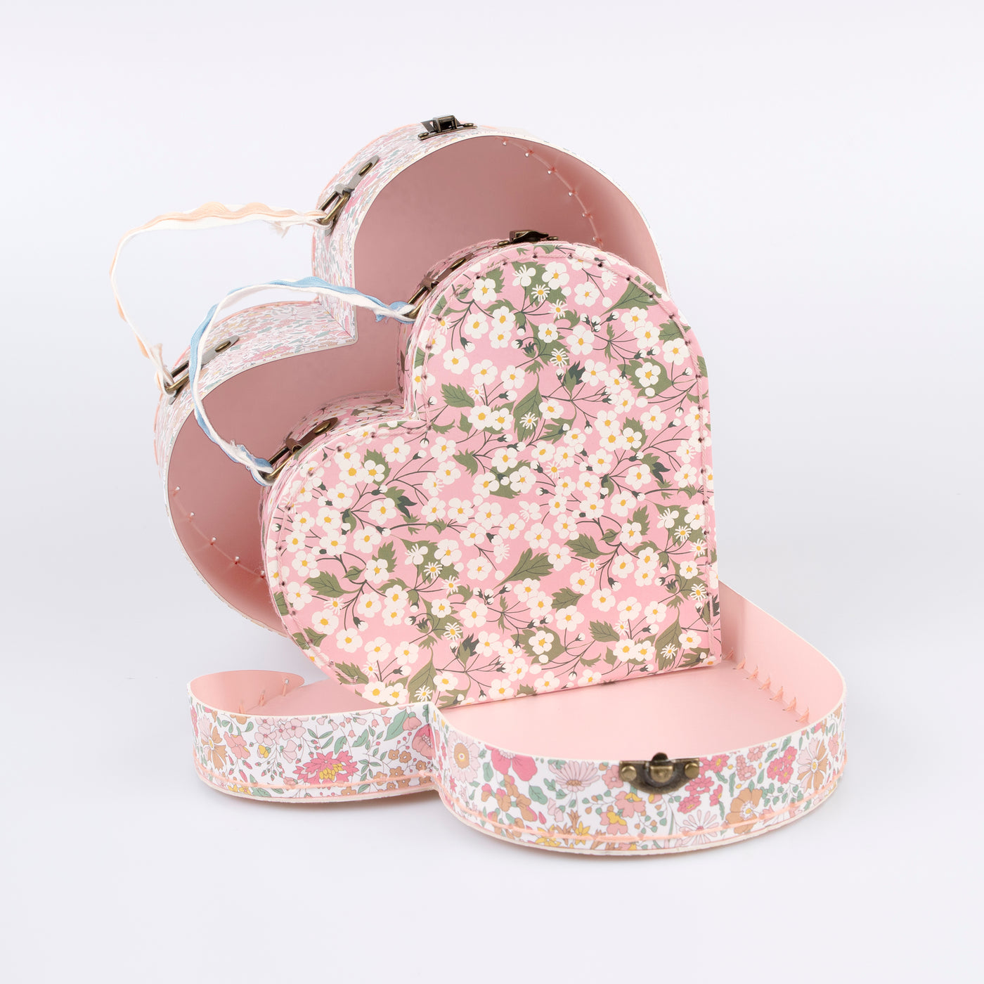 Two different sized heart-shaped suitcases made from stitched card with lamination. The smaller case can be stored inside the larger.  Each suitcase features a different Liberty floral print design, with pink tones, on the outside.