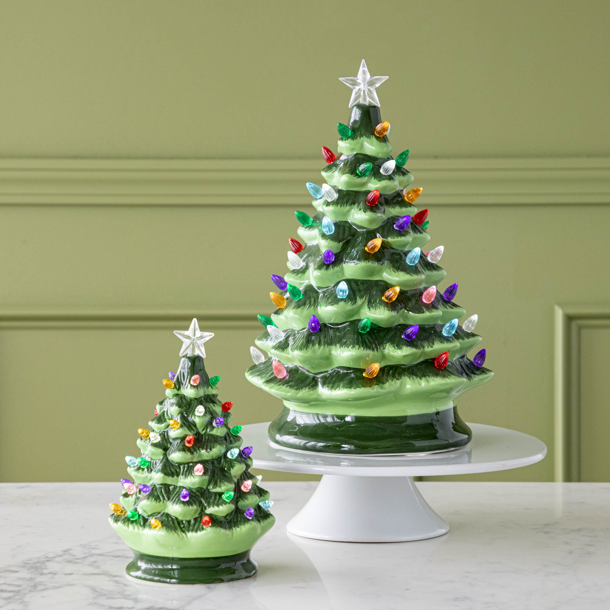 Two Porcelain Vintage Lit Trees with Timers; one on a cake stand and one on a marble table.