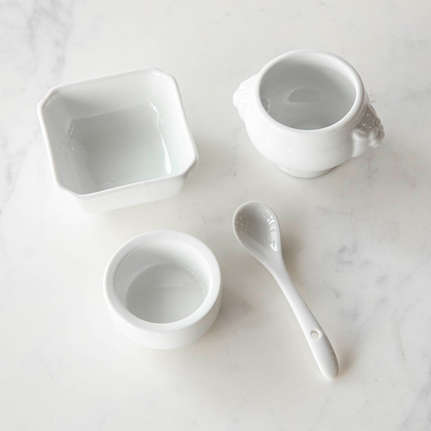 Three White Porcelain Mini Bowls with assorted spices and a spoon on a marble surface by BIA.