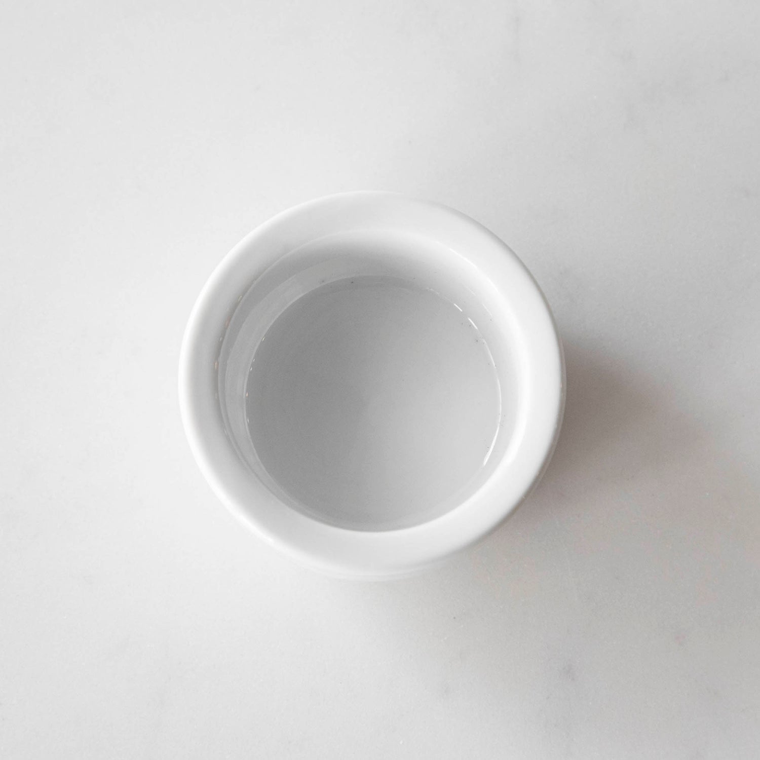 Three White Porcelain Mini Bowls with assorted spices and a spoon on a marble surface by BIA.