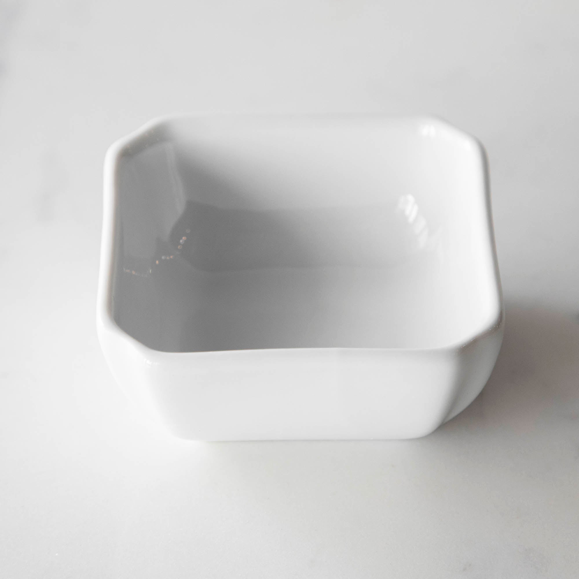 Three White Porcelain Mini Bowls with assorted spices and a spoon on a marble surface by BIA.