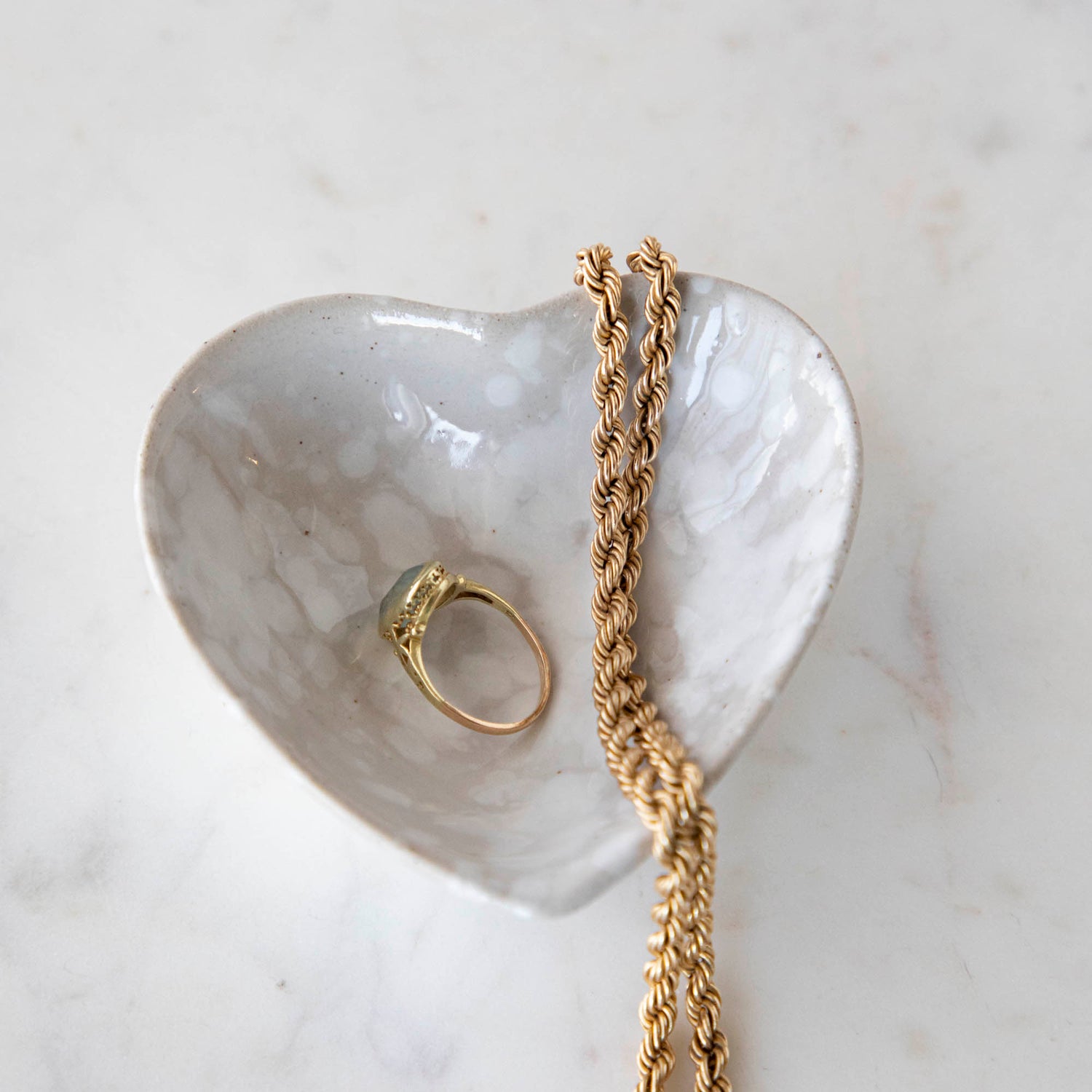 A Creative Co-Op Stoneware Heart Dish with a gold ring and a gold chain.