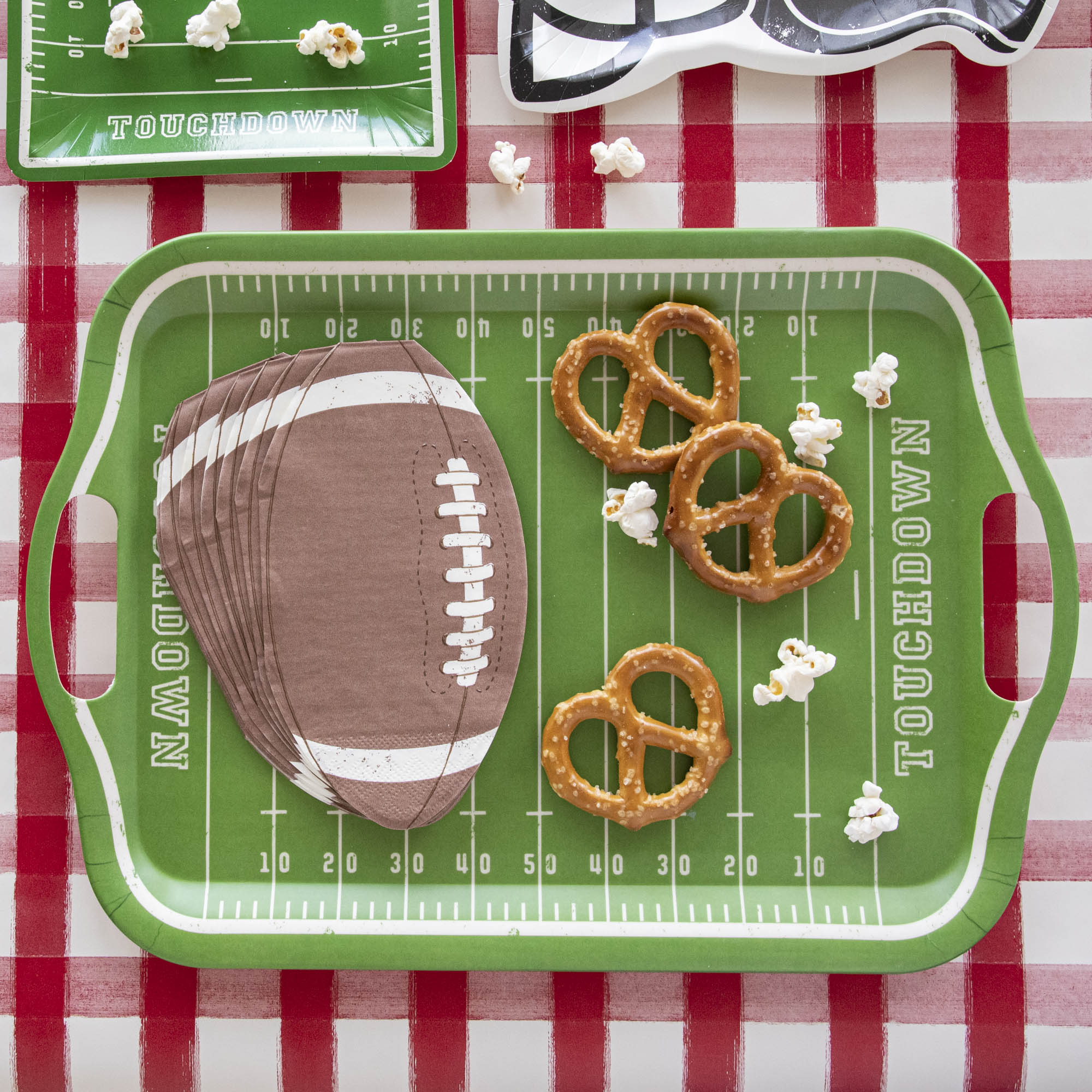 Die-cut football paper napkins on a football field tray surrounded by pretzels and popcorn.