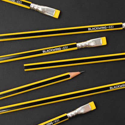 A collection of Blackwing Volume 651- Tribute to Bruce Lee pencils, one sharpened, arranged diagonally on a dark background, reminiscent of Bruce Lee&