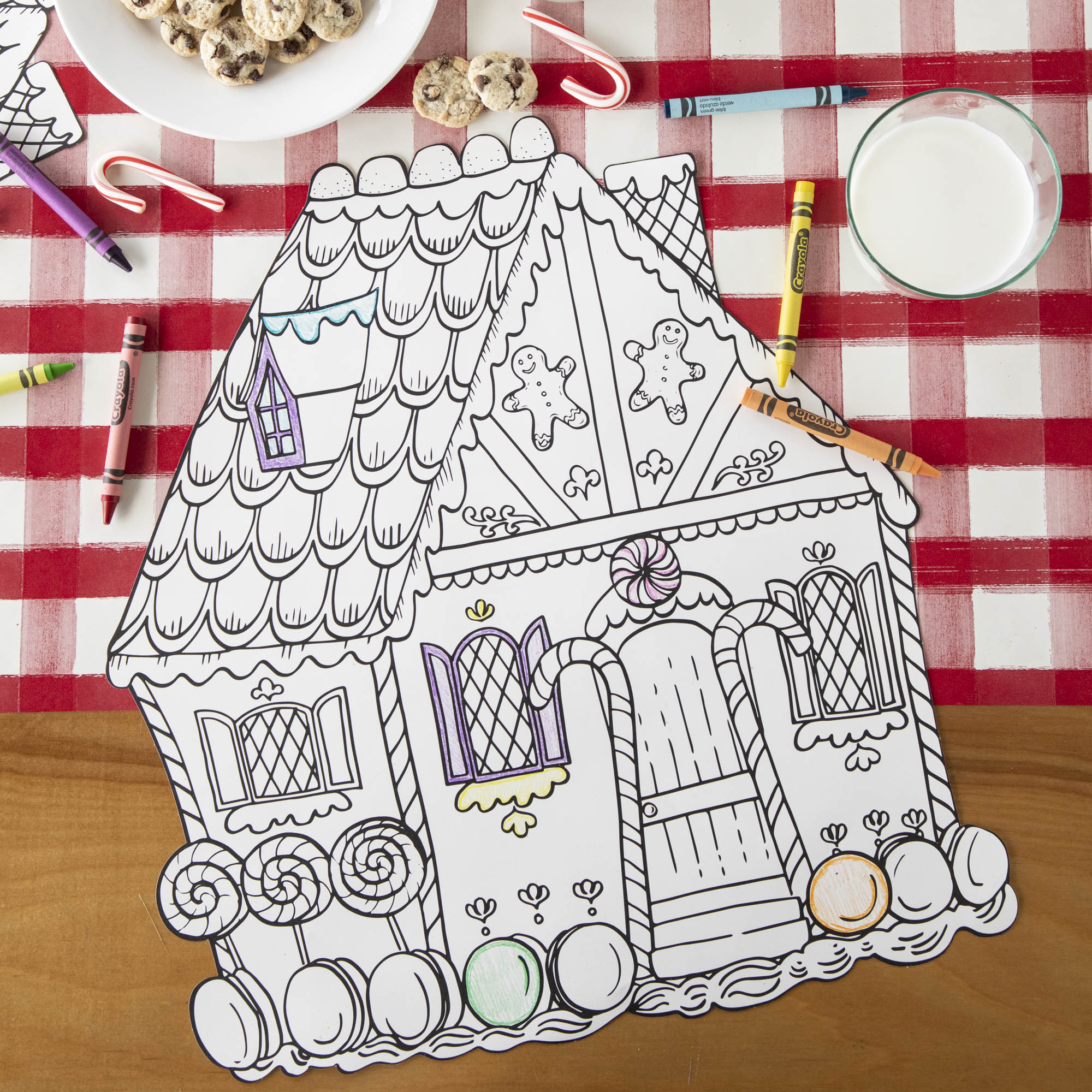 A Die-cut Gingerbread House Coloring Placemat on a Christmas-themed activity table with crayons.