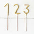 Three Tops Malibu Gold Number Cake Topper Sparklers sticks on a wooden surface, instantly transforming any celebration into an elegant affair. These 4" tall decorations capture attention with a sparkling golden finish.