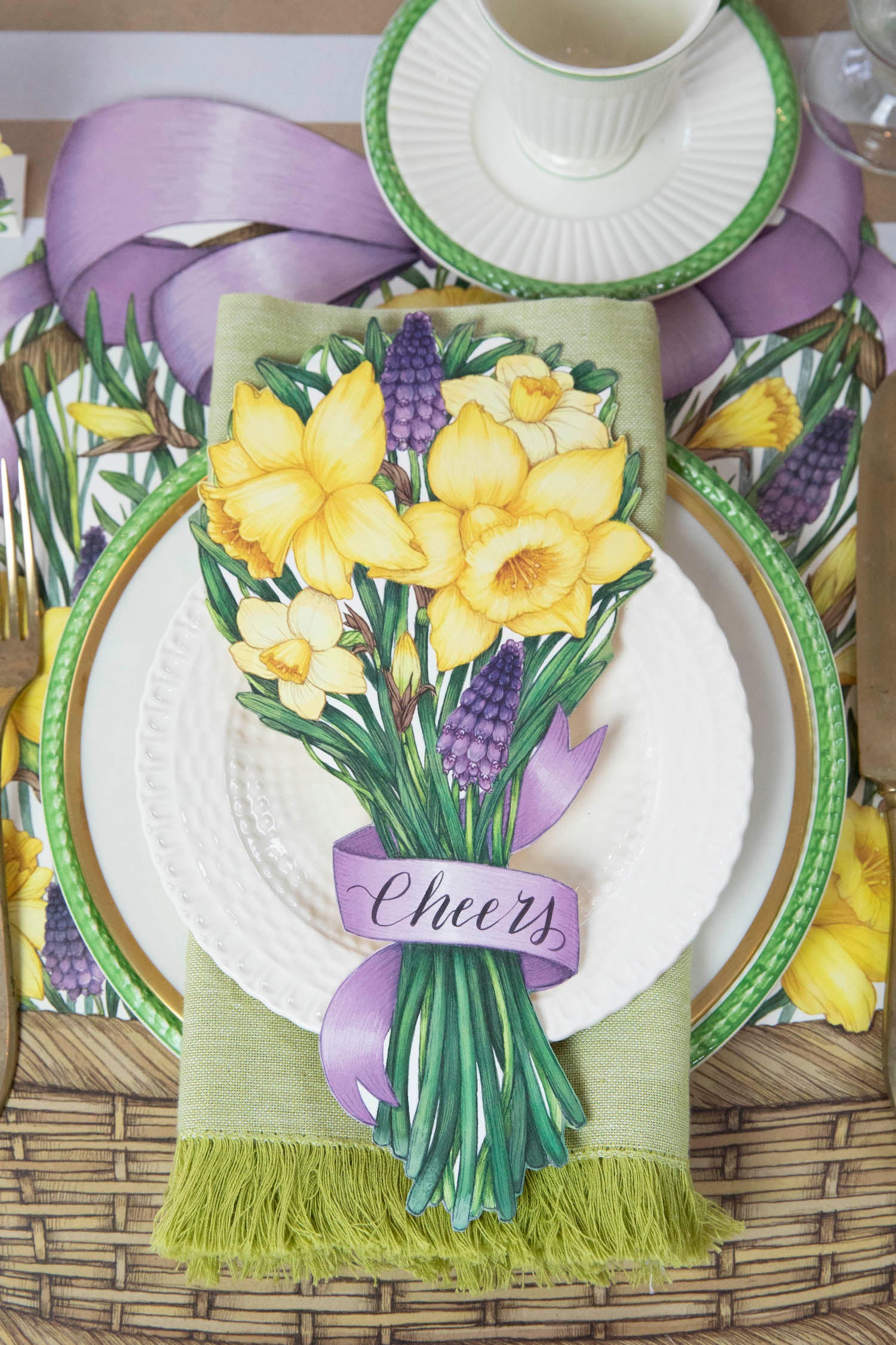 Top-down view of a floral place setting featuring a Daffodil Table Accent with &quot;Cheers&quot; written on the ribbon resting on the plate.