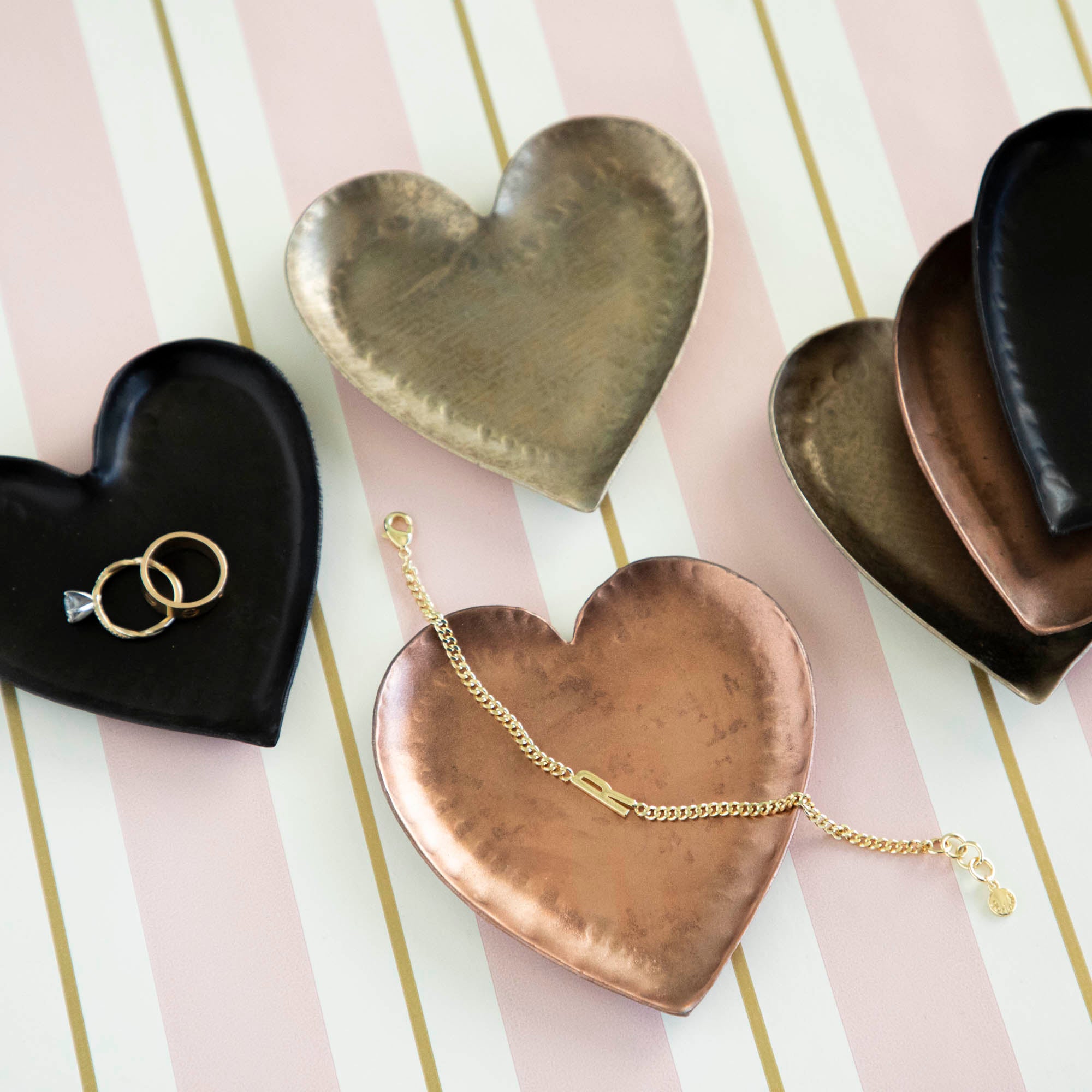 A HomArt Forged Iron Heart Tray with gold and silver rings on a copper-colored, pink, and white striped surface.