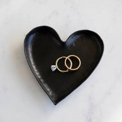 A HomArt Forged Iron Heart Tray with gold and silver rings on a copper-colored, pink, and white striped surface.