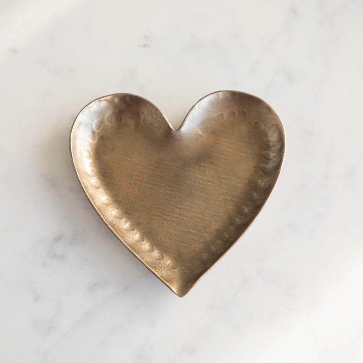 A HomArt Forged Iron Heart Tray with gold and silver rings on a copper-colored, pink, and white striped surface.