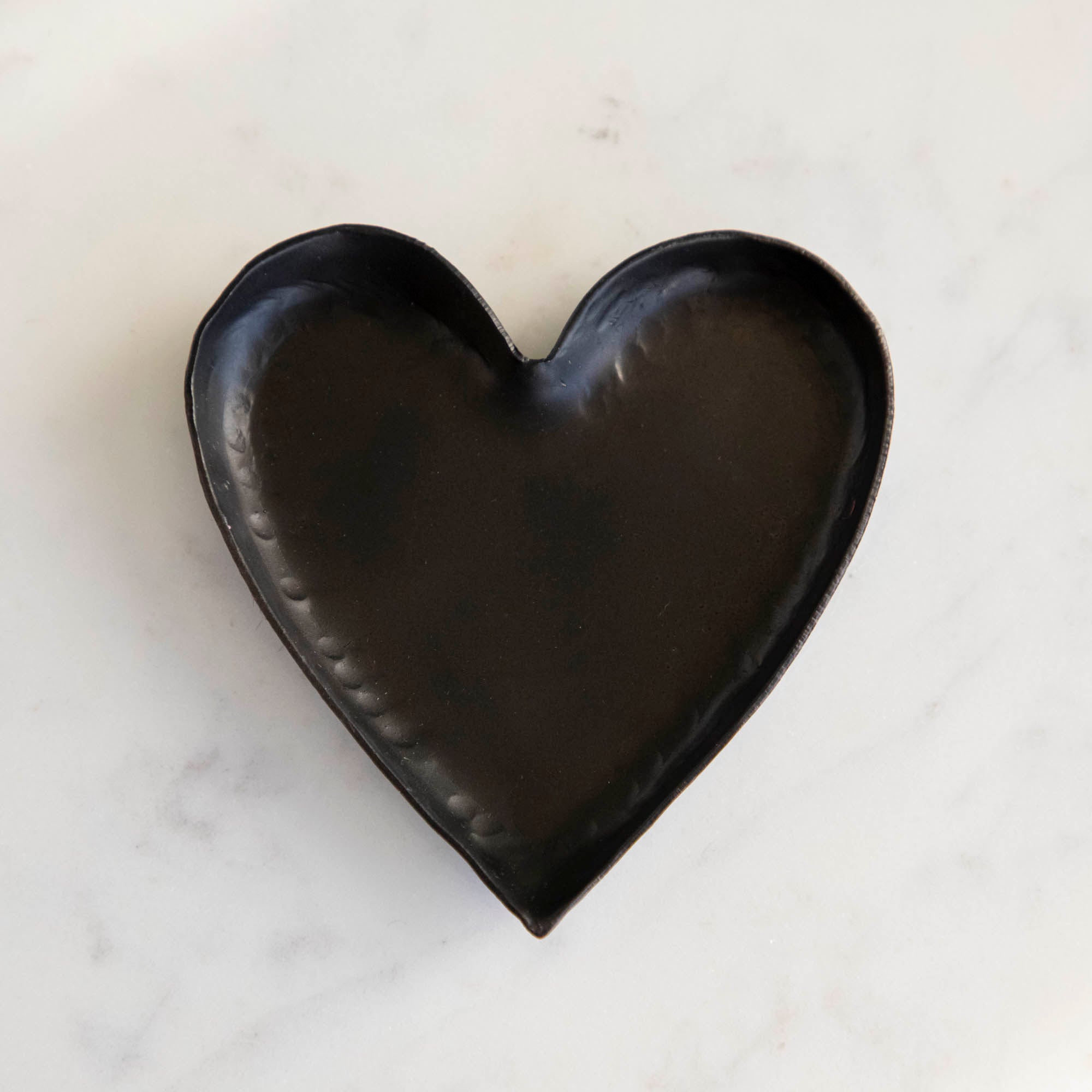 A HomArt Forged Iron Heart Tray with gold and silver rings on a copper-colored, pink, and white striped surface.