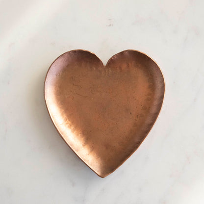 A HomArt Forged Iron Heart Tray with gold and silver rings on a copper-colored, pink, and white striped surface.