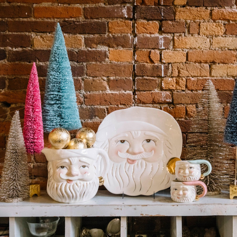 A display of the Papa Noel Cookie Platter, Pitcher and 2 mugs on a shelf with Christmas decor.