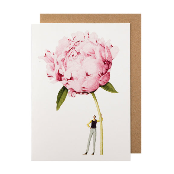 A white greeting card featuring a stylized illustration of a man holding a gigantic pink peony bloom by the stem, with the included kraft paper envelope tucked behind. 