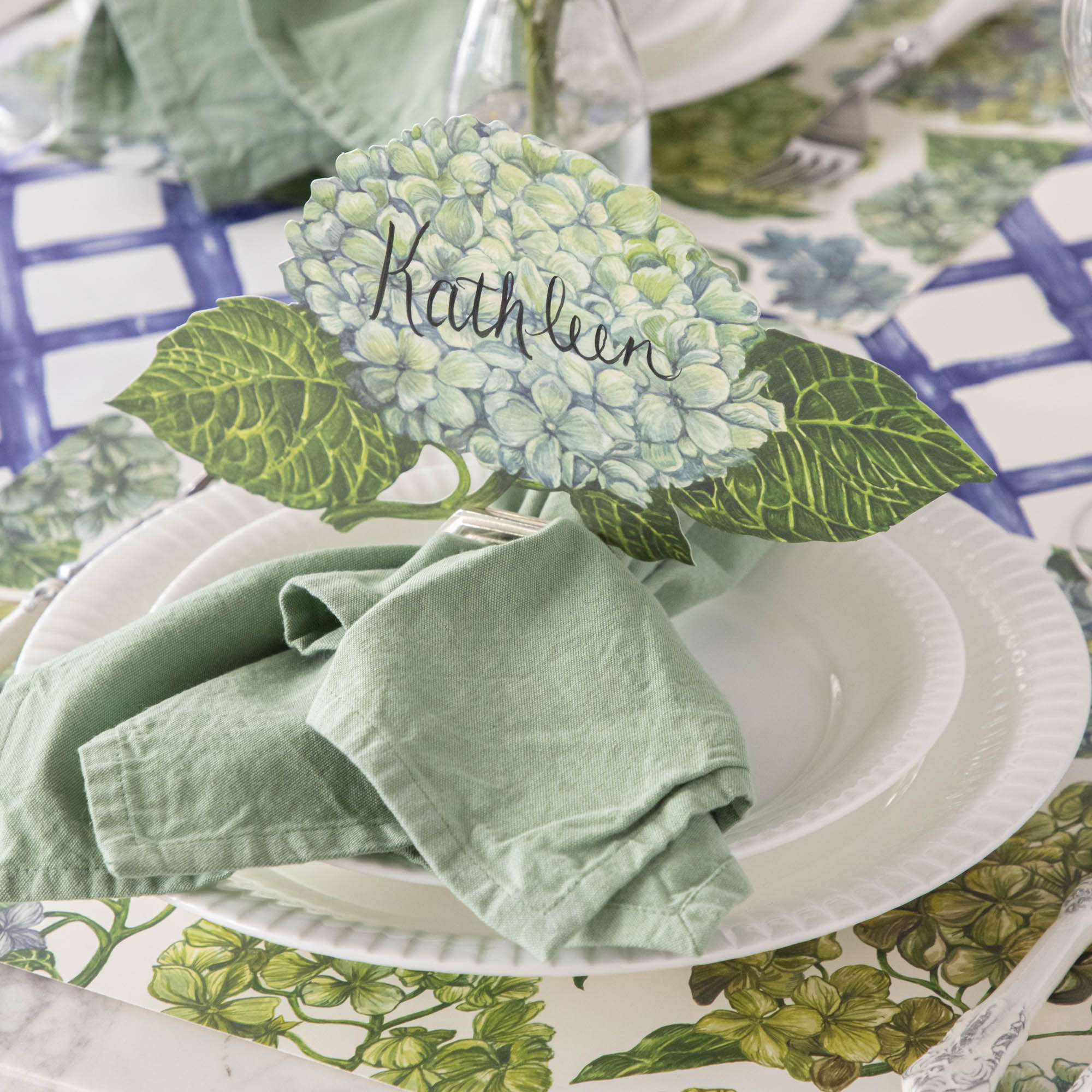 An elegant floral place setting featuring a Hydrangea Table Accent labeled &quot;Kathleen&quot; in a napkin ring card holder.