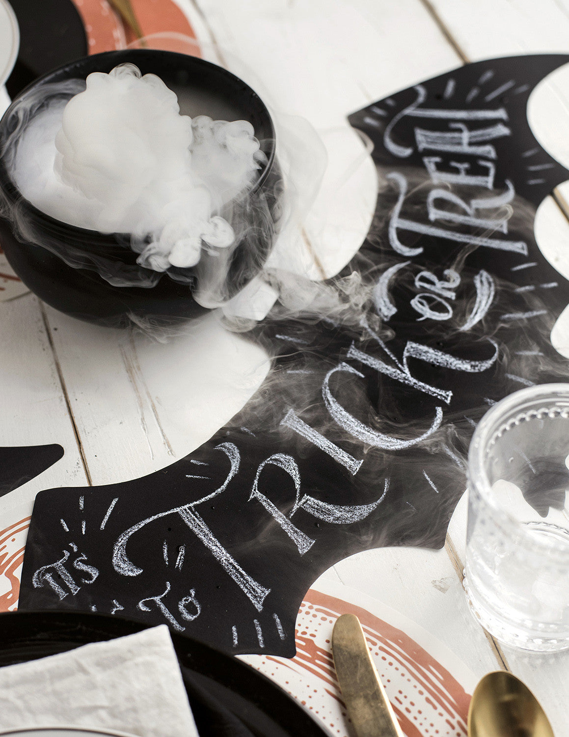 The Die-cut Bat Placemat on a spooky Halloween table setting, with &quot;Trick or Treat&quot; hand-written on it in white chalk.