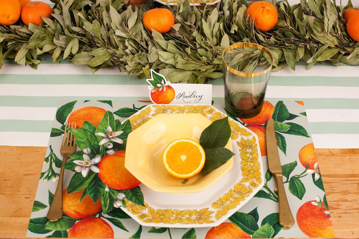 A vibrant citrus-themed place setting featuring an Orange Orchard Place Card reading &quot;Audrey&quot; standing behind the plate.