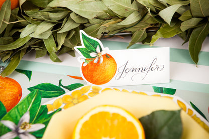 Close-up of an Orange Orchard Place Card reading &quot;Jennifer&quot; standing behind the plate of an elegant place setting.