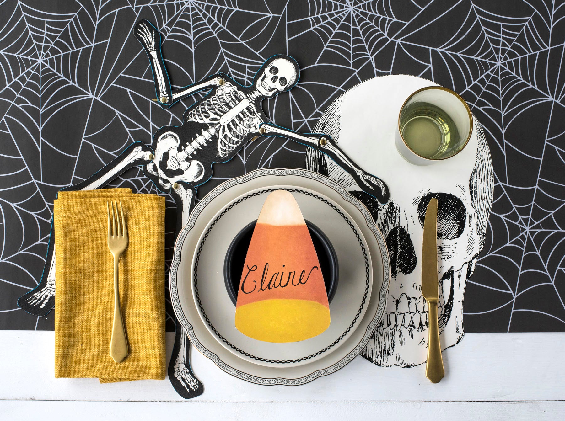 A spooky Halloween place setting featuring an Articulated Skeleton Decorative Accent on the table with its arm around the plate.