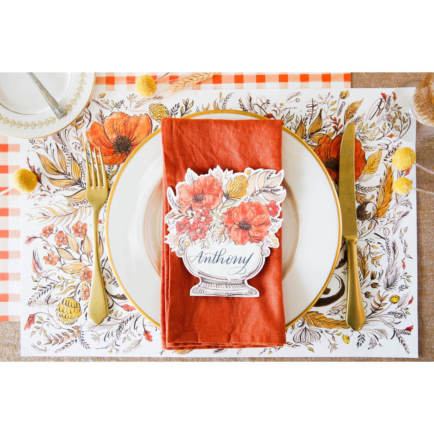 Top-down view of an elegant Thanksgiving place setting featuring an Autumn Arrangement Place Card reading &quot;Anthony&quot; laying flat on the plate.